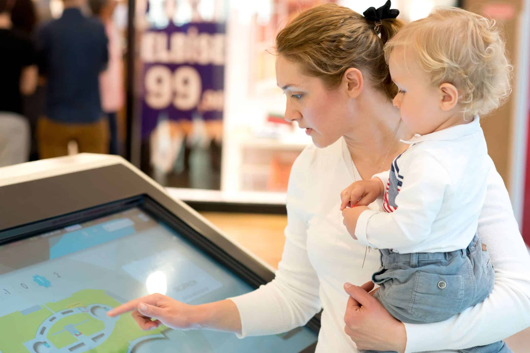 lady using an digital wayfinding kiosk while holding a young child.